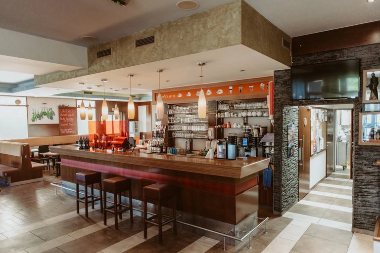 Innenraum des Restaurant Simperl mit langer Holztheke, Barhockern, hängenden Pendelleuchten und Sitznischen im Hintergrund.