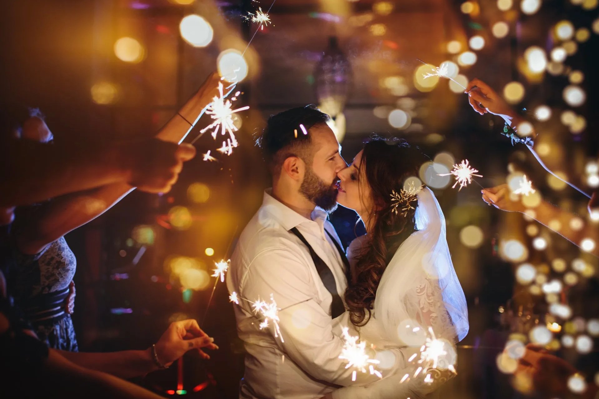 Braut und Bräutigam küssen sich umgeben von Gästen, die Funkelkerzen halten.