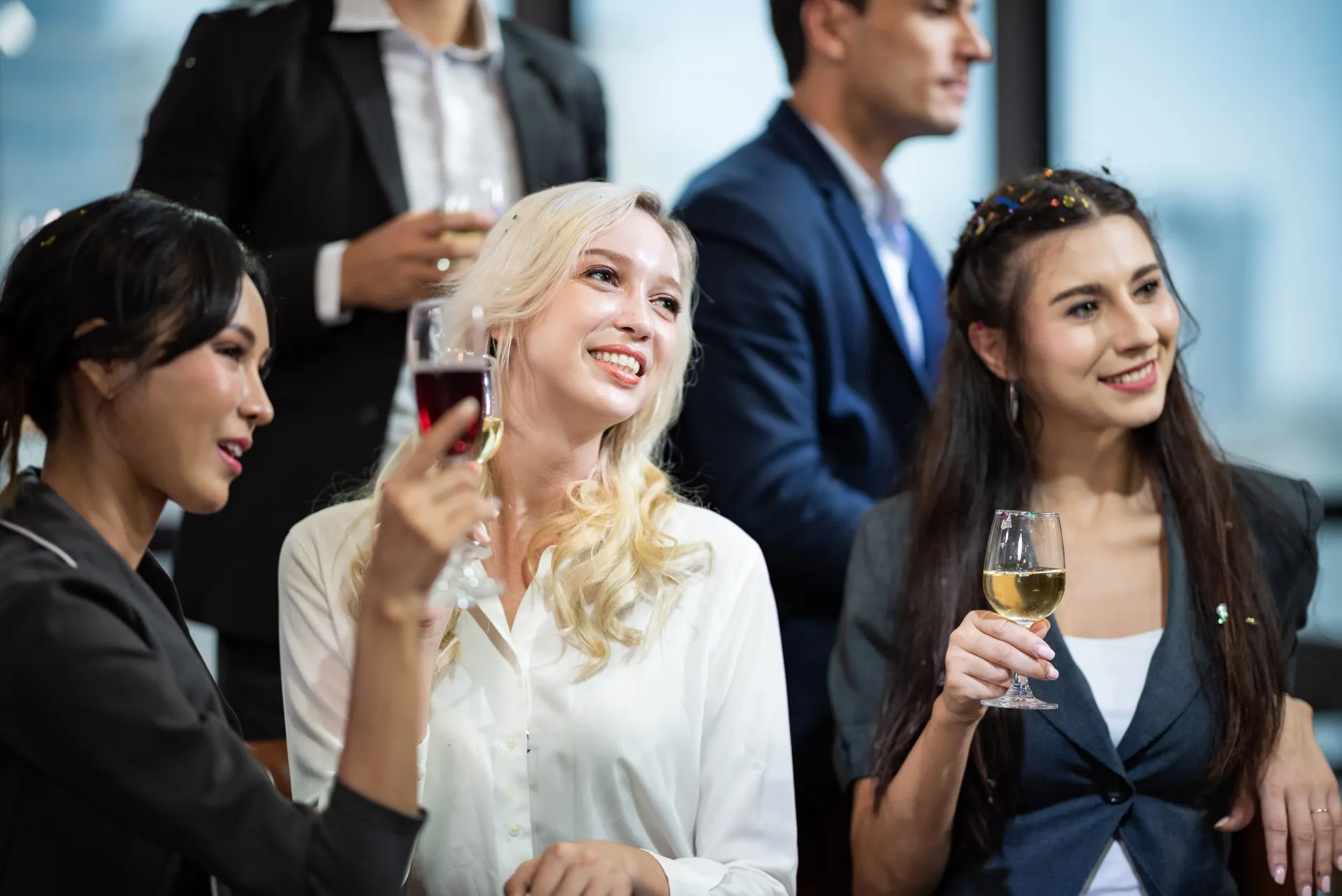 Drei stilvoll gekleidete Gäste stoßen mit Weingläsern an.