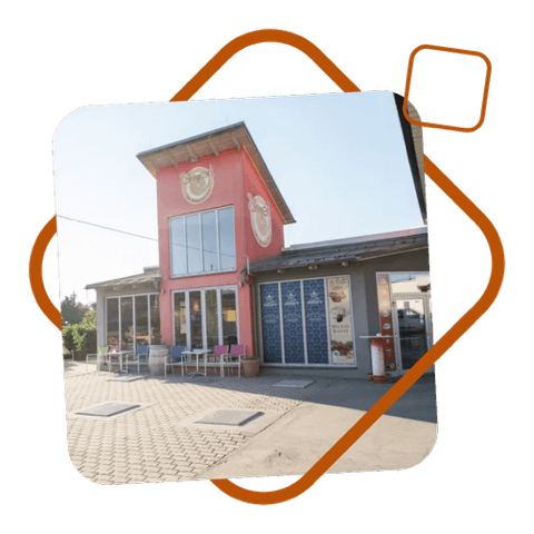 Fassade des Restaurant Simperl mit rotem Turm, großen Glasfenstern und Außensitzplätzen auf gepflastertem Platz.